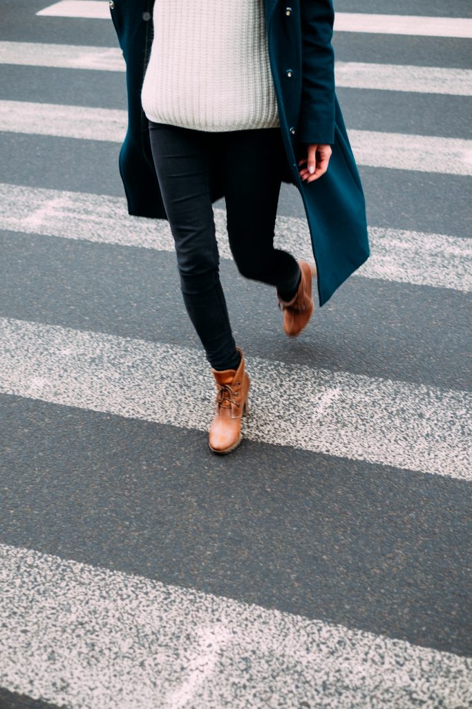 femme portant un jean noir un pull clair des bottines marron et un manteau long sombre